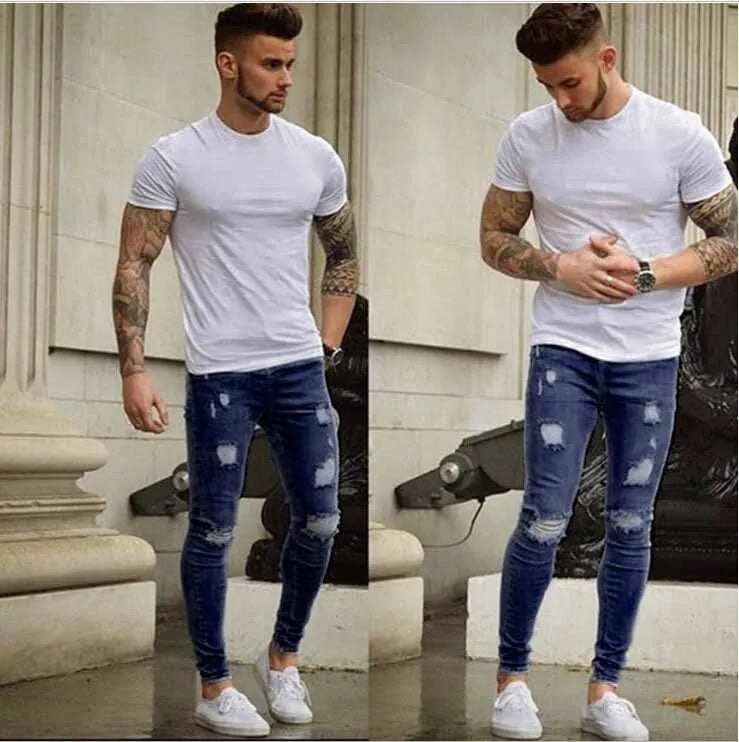 Frayed slim-fit jeans in blue, showing distressed hem and slim leg shape, on a model standing casually