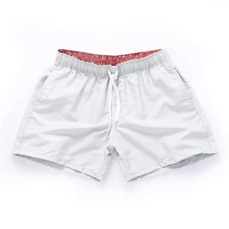 Men's straight-leg polyester surf shorts on a beach, showing colour options like black, fluorescent yellow, and navy blue.