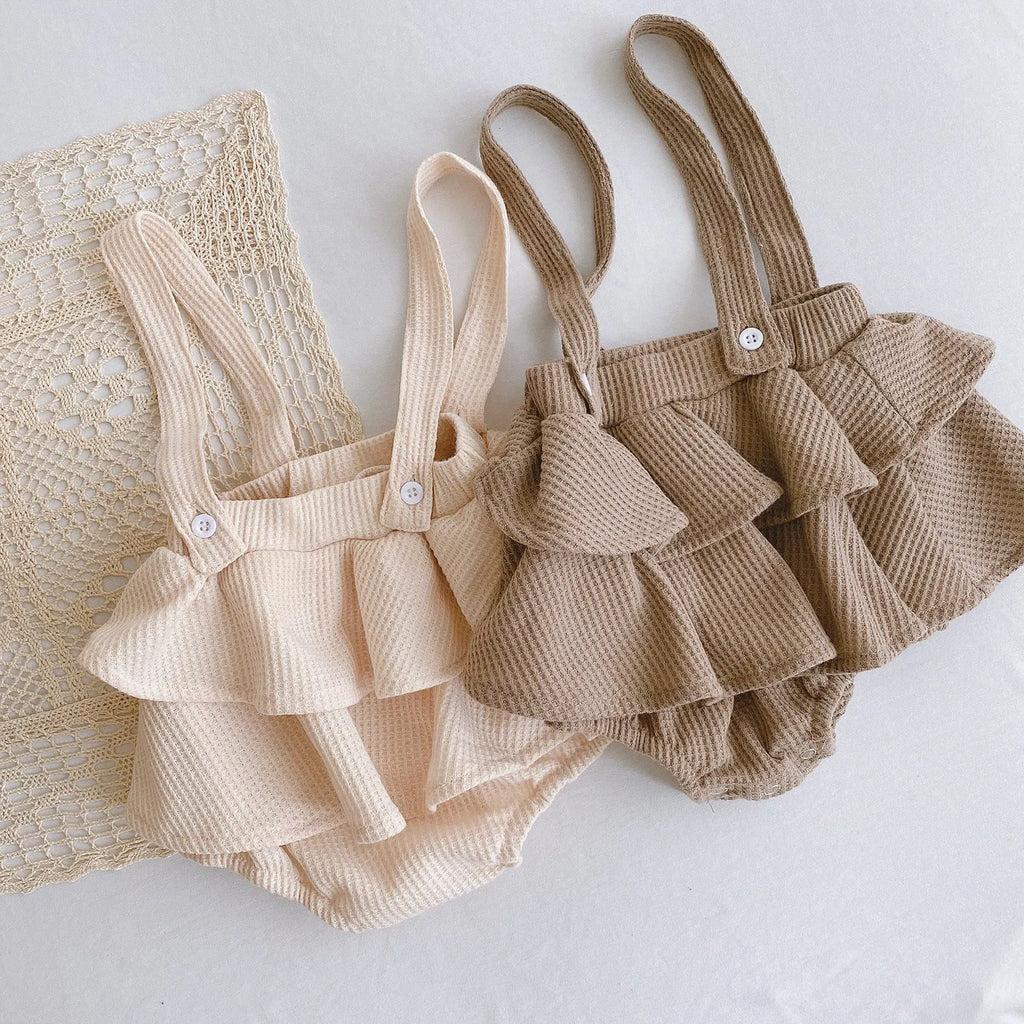 Baby girl wearing a cotton pleated skirt romper with lotus leaf sling design in apricot colour