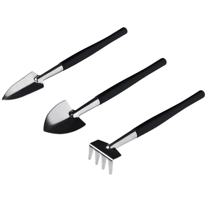 Black plastic and metal mini garden tool set for succulents, including small shovel, tweezers, brushes, bottle, and a square cushion.