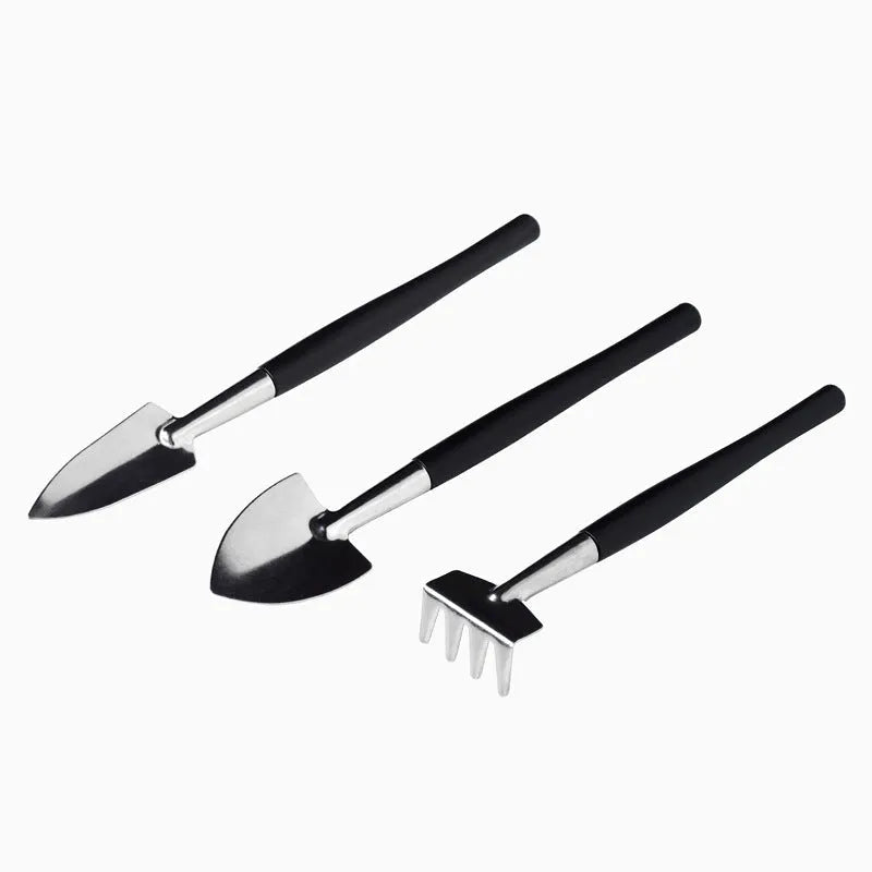 Black plastic and metal mini garden tool set for succulents, including small shovel, tweezers, brushes, bottle, and a square cushion.