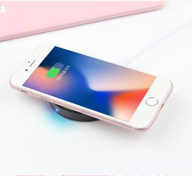 Square Qi wireless charging pad on a table next to a mobile phone.
