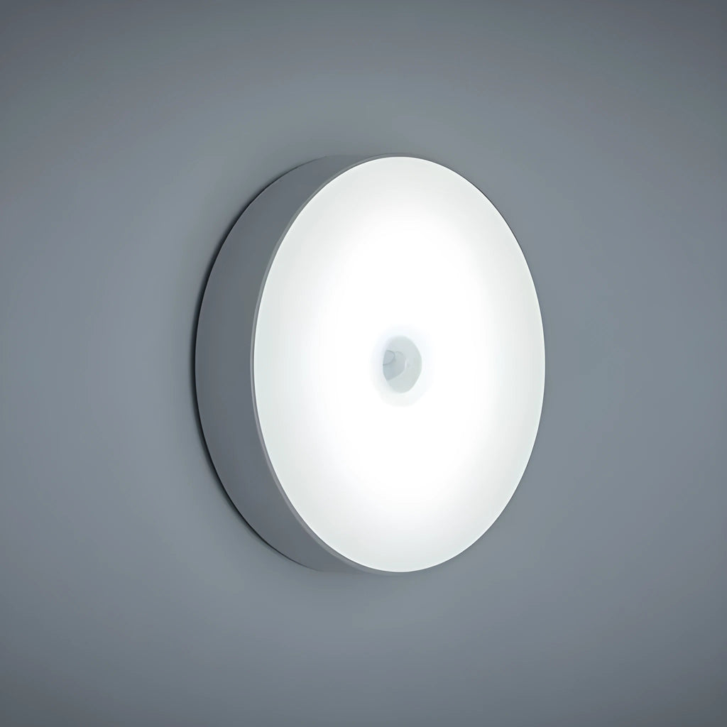 Small circular white USB-rechargeable motion sensing LED night light with adhesive backing.