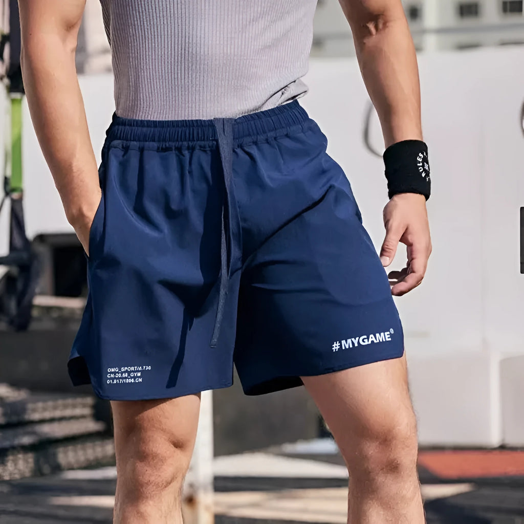 Men's grey fitness shorts with a four-point training design, shown on a model, highlighting the short length and elastic fabric.