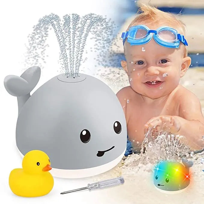 Grey and white cartoon whale bath toy spraying water with LED lights illuminated on water surface.