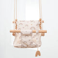 Cotton canvas baby swing chair with wooden frame and cushion, hanging with decorative tassels.