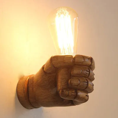 Close-up of a black resin wall lamp shaped like a clenched fist, mounted on a textured wall.
