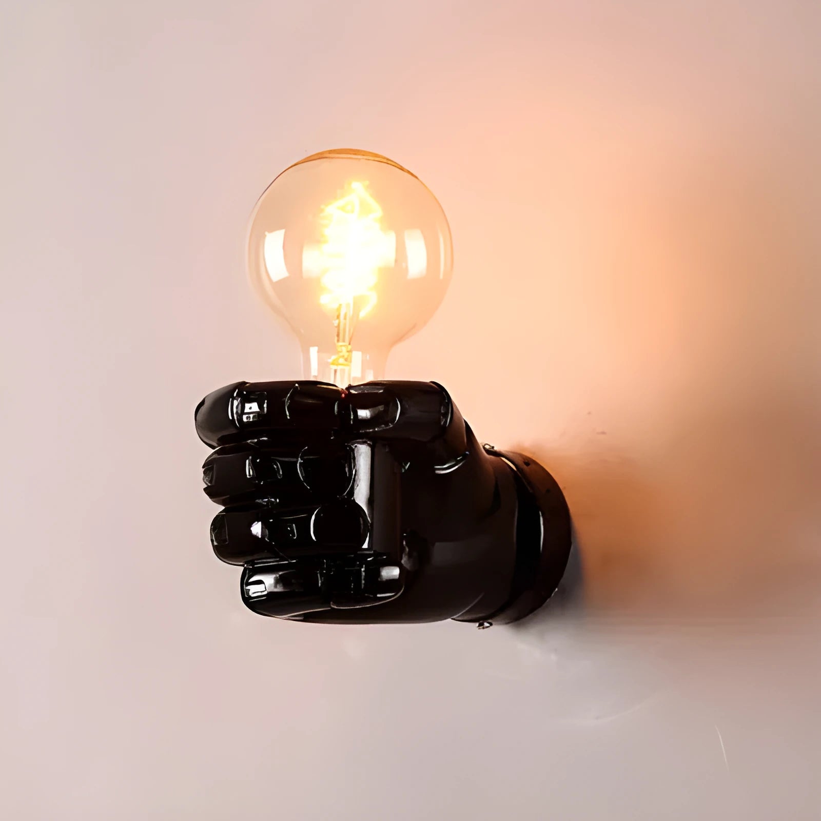Close-up of a black resin wall lamp shaped like a clenched fist, mounted on a textured wall.