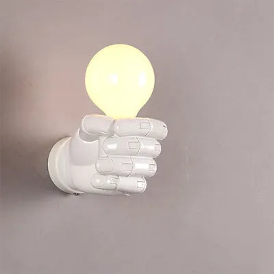 Close-up of a black resin wall lamp shaped like a clenched fist, mounted on a textured wall.