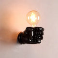 Close-up of a black resin wall lamp shaped like a clenched fist, mounted on a textured wall.