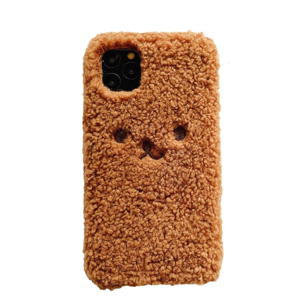 Brown embroidered plush bear face on a clear TPU iPhone case, showing precise cutouts for camera and ports.