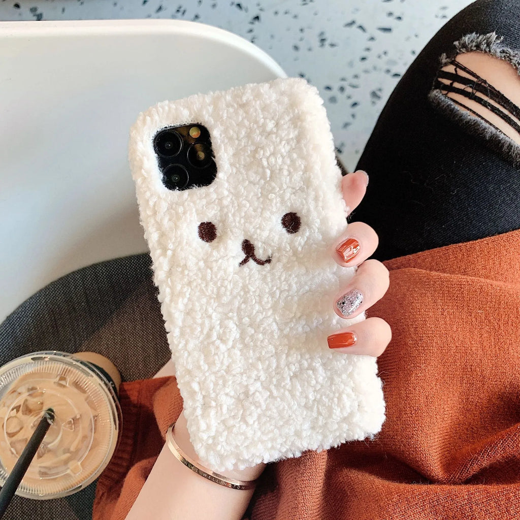 Brown embroidered plush bear face on a clear TPU iPhone case, showing precise cutouts for camera and ports.