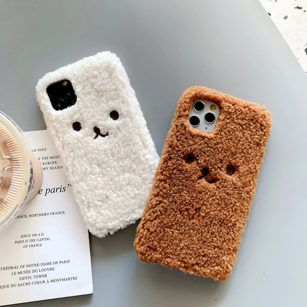 Brown embroidered plush bear face on a clear TPU iPhone case, showing precise cutouts for camera and ports.