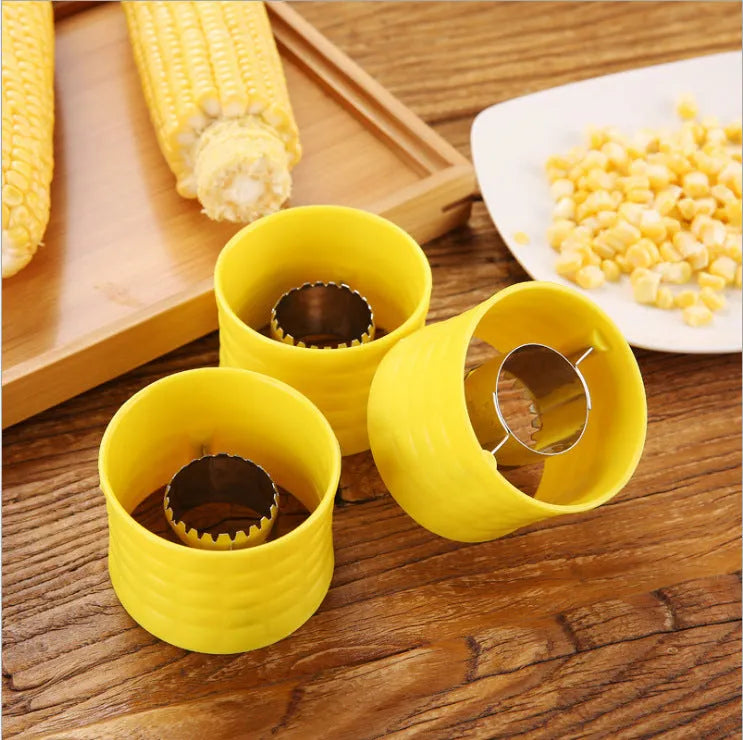Yellow manual corn thresher kitchen tool with a corn-shaped plastic body and visible stainless steel gear.