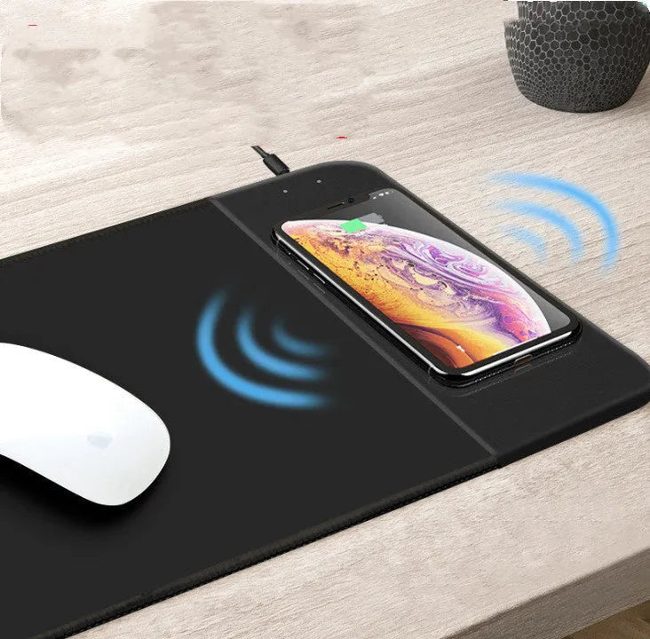 Black wireless charging mouse pad with RGB edge lighting on a desk.