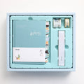 Peekaboo gift box containing a 13x18 cm hand ledger notebook and a pen, with a paper cover in a random colour.