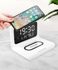 White wireless charger alarm clock showing time, date, and temperature on its display with a phone charging on top.
