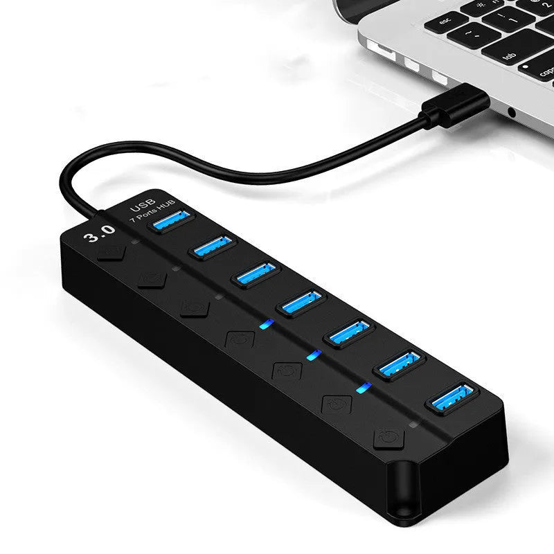 Black 7-port USB 3.0 hub with external power adapter and 1-metre cable on a desk