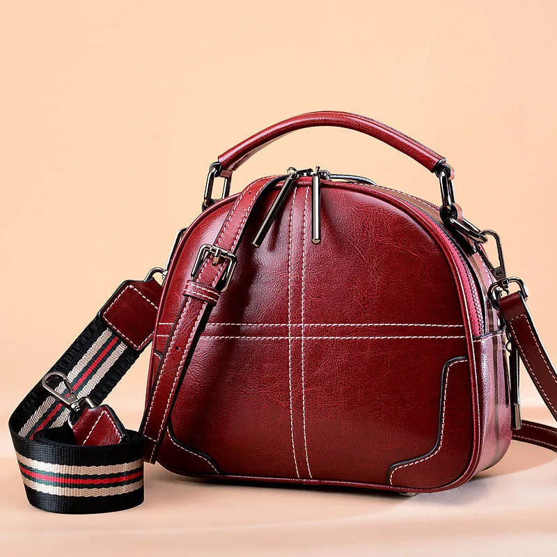 Round leather handbag in cowhide with a zipper and soft handle, shown in wine red colour.