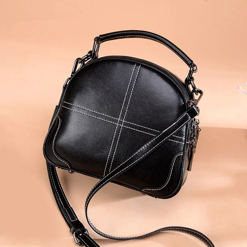 Round leather handbag in cowhide with a zipper and soft handle, shown in wine red colour.