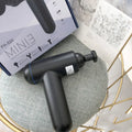 Black fascia massage gun with three metal attachment heads on a table.