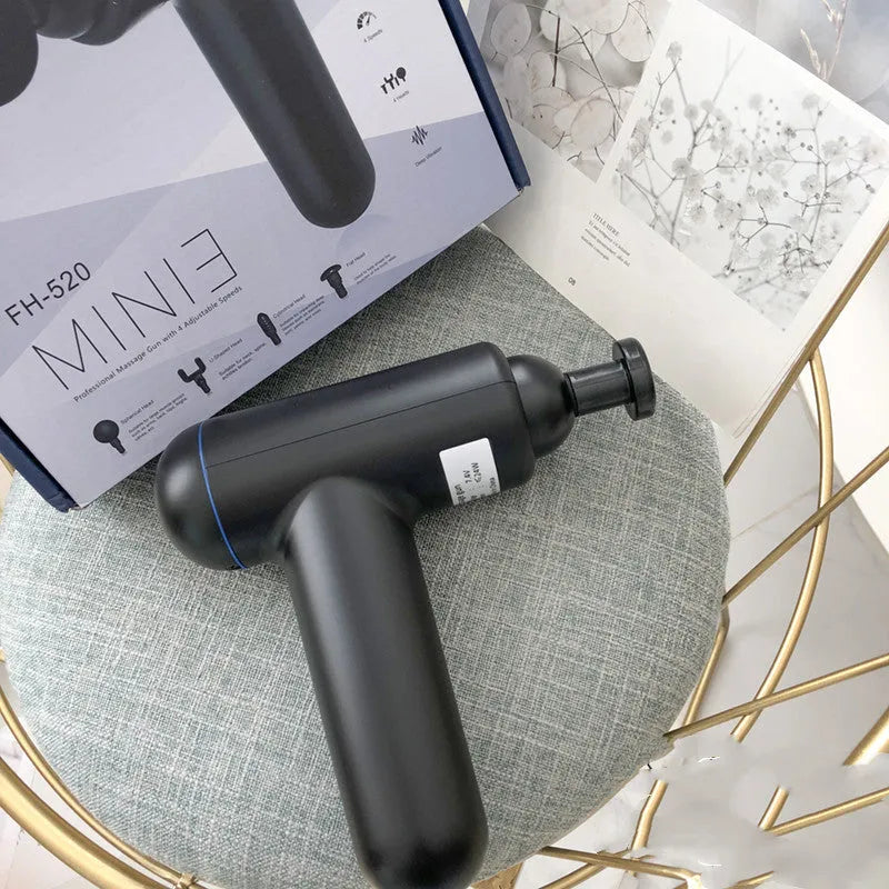 Black fascia massage gun with three metal attachment heads on a table.
