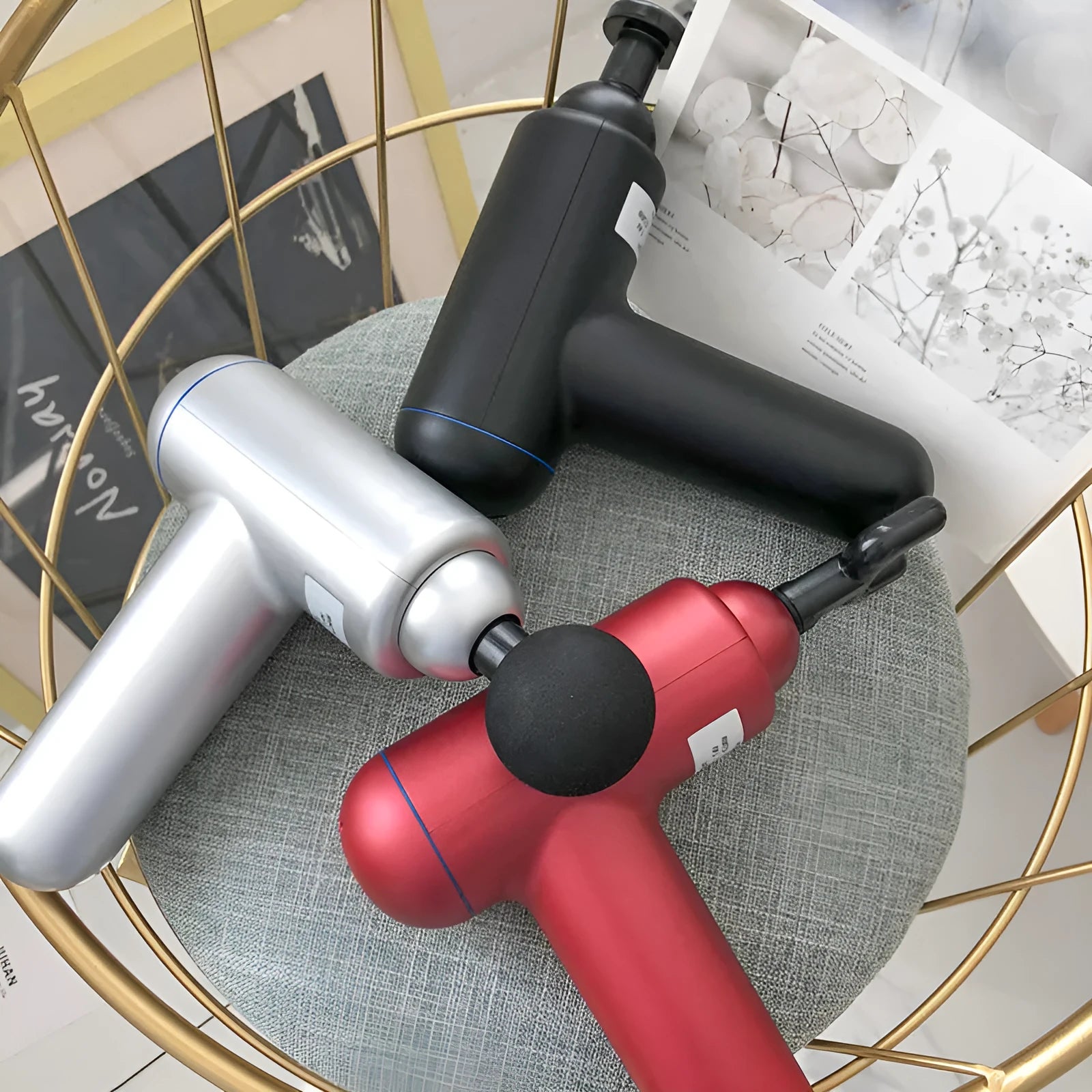 Black fascia massage gun with three metal attachment heads on a table.