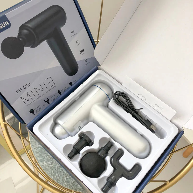 Black fascia massage gun with three metal attachment heads on a table.