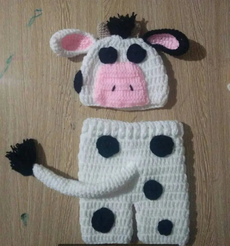 Hand-knitted white baby cow suit set with matching hat and pants on a newborn