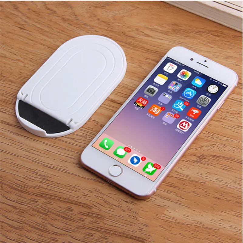 Plastic lazy bracket mobile phone stand in multiple colour choices on a table.