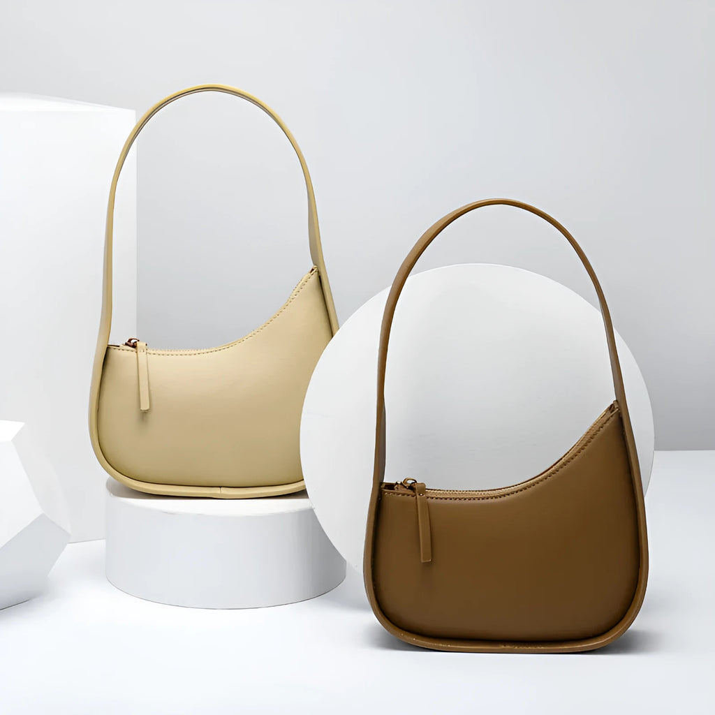 Small half moon shaped leather women's shoulder bag with a wide strap, shown in light brown.