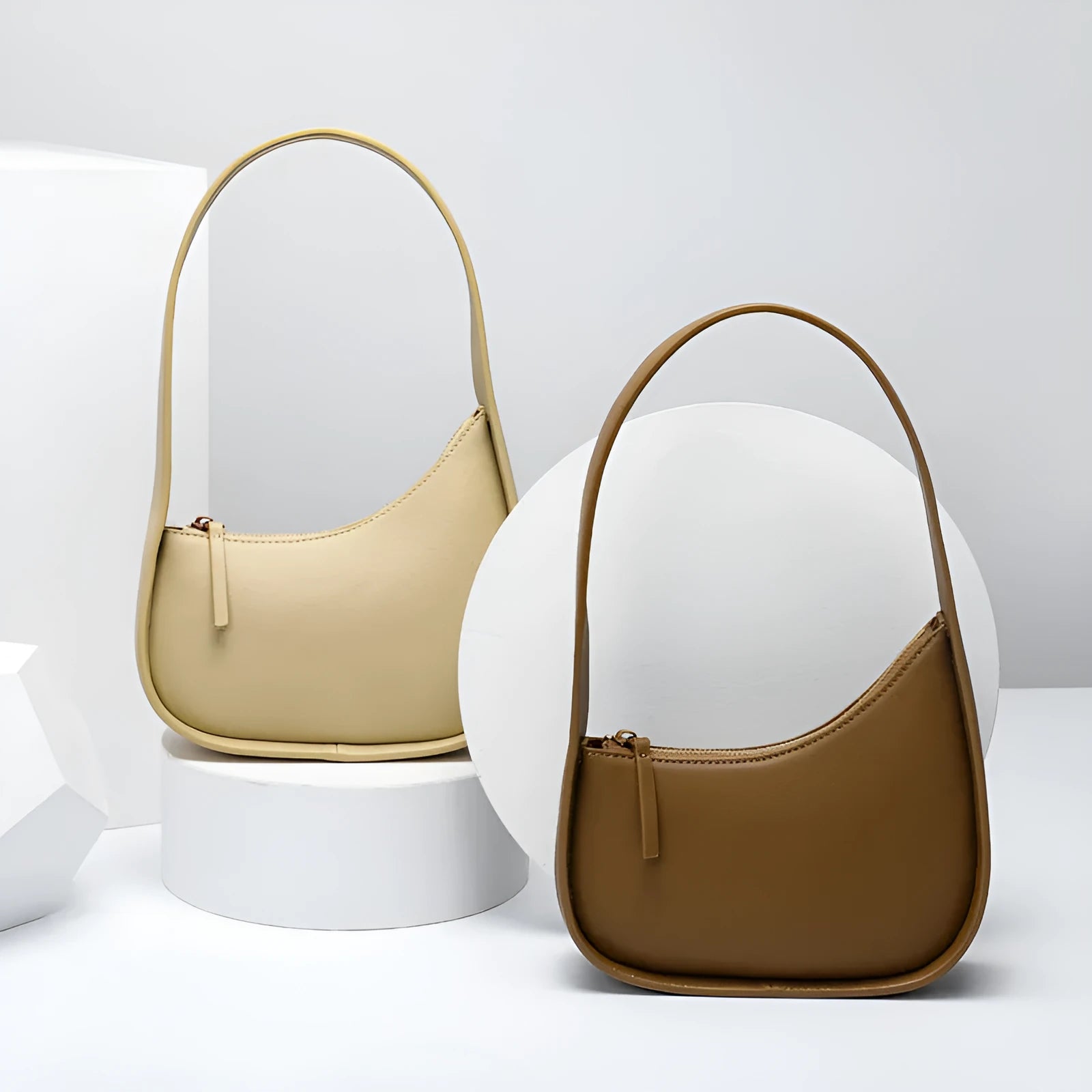 Small half moon shaped leather women's shoulder bag with a wide strap, shown in light brown.