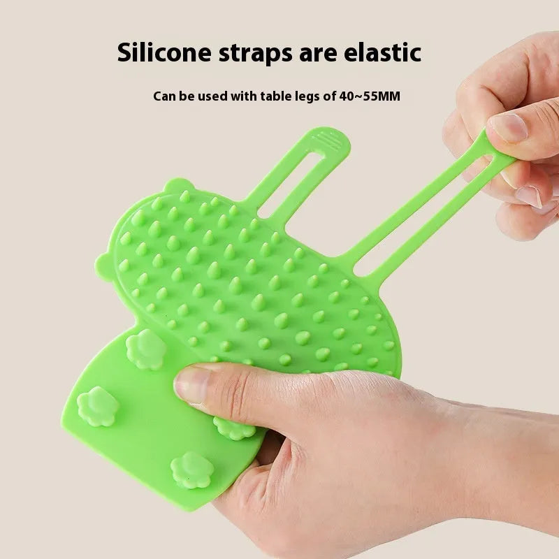 Silicone cat grooming comb with rounded teeth and adjustable strap mounted on a table leg.