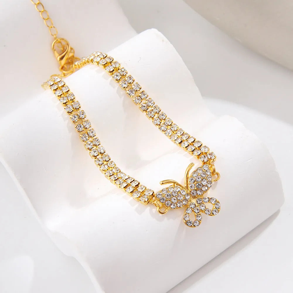 Gold rhinestone butterfly anklet with bow shape and gemstone inlay on white background