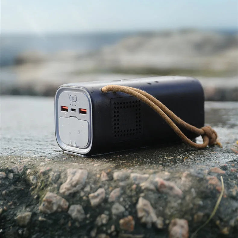 Black portable power bank with 220V socket, digital display, and solar panel on a wooden table.