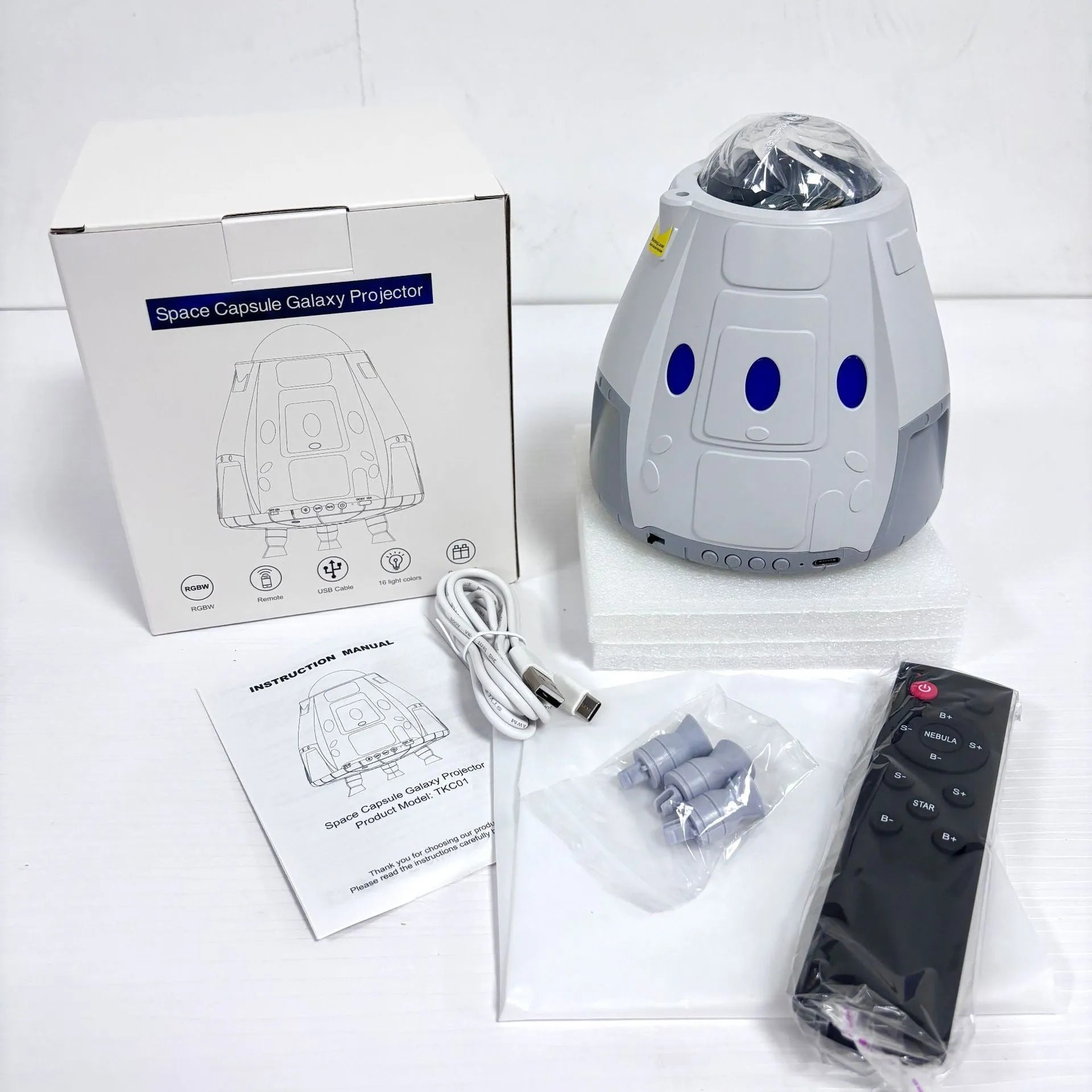 Space capsule shaped USB galaxy projection lamp with remote control on a desk.
