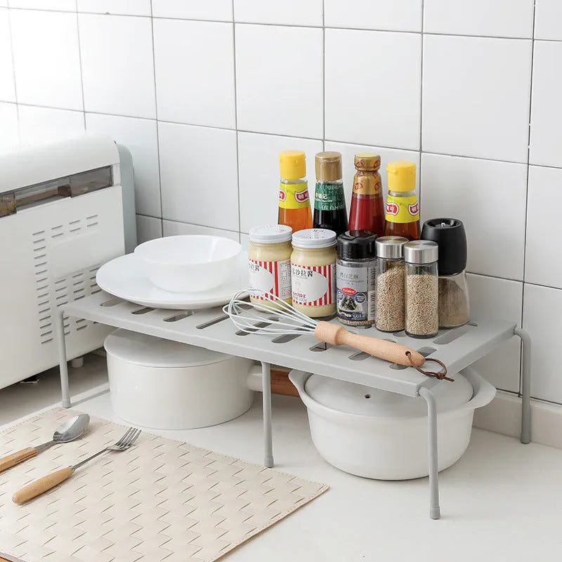 White telescopic plastic kitchen rack with single shelf, shown at adjusted height on a kitchen floor.