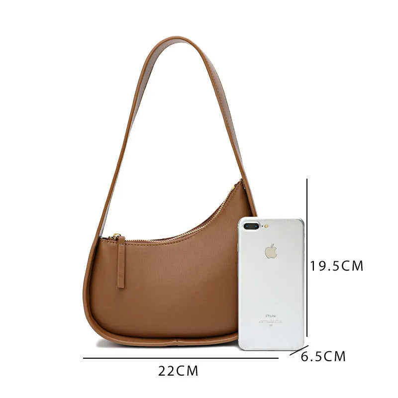 Small half moon shaped leather women's shoulder bag with a wide strap, shown in light brown.