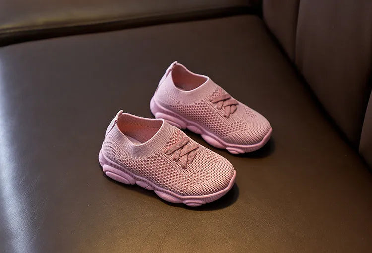 Children's white fabric lazy slip-on shoe with non-slip rubber sole on a wooden floor.