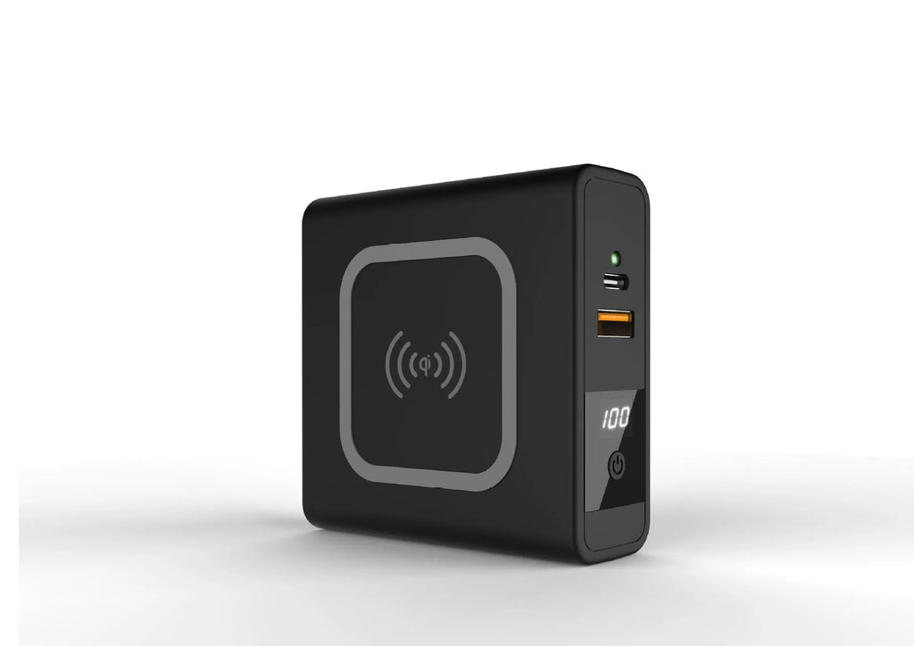 Black Super QI wireless power bank with integrated folding plug shown on a table next to a smartphone.