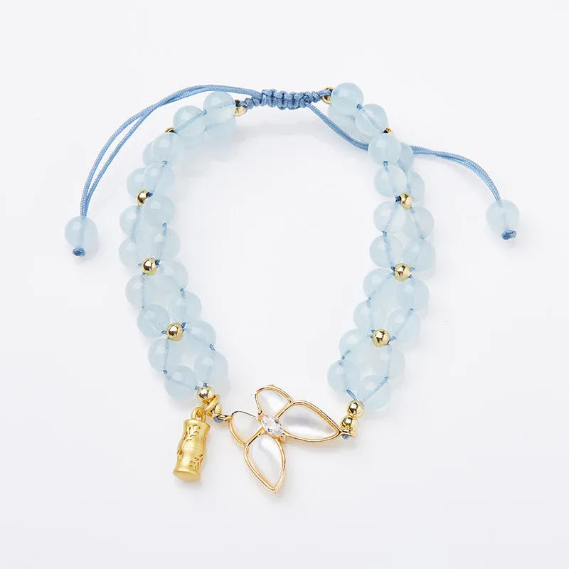 Close-up of a women's woven bracelet with 6mm aquamarine beads and a butterfly charm on a wrist.