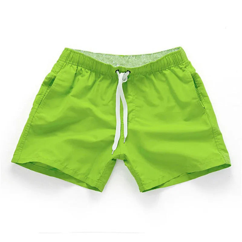 Men's straight-leg polyester surf shorts on a beach, showing colour options like black, fluorescent yellow, and navy blue.