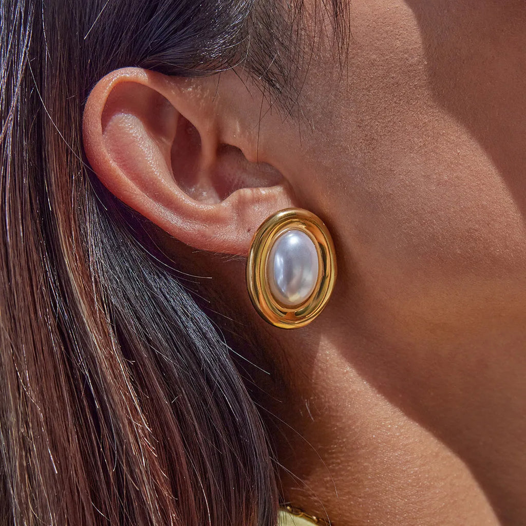A pair of small stainless steel ear studs with a vintage-style pearl decoration on a silver-coloured base.
