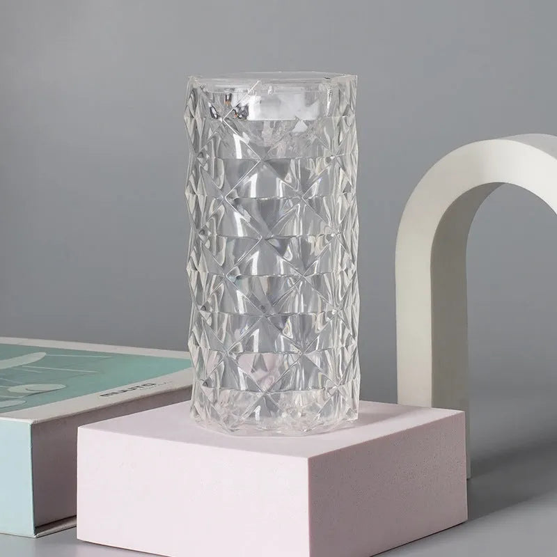 Rose atmosphere crystal bedside lamp with plastic lampshade emitting soft yellow light on a wooden table