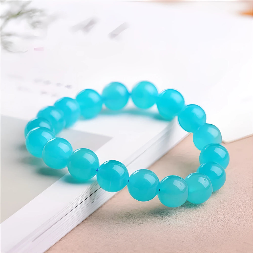 A selection of loose, polished ice-blue Amazonite beads in various sizes next to a finished crystal bracelet.
