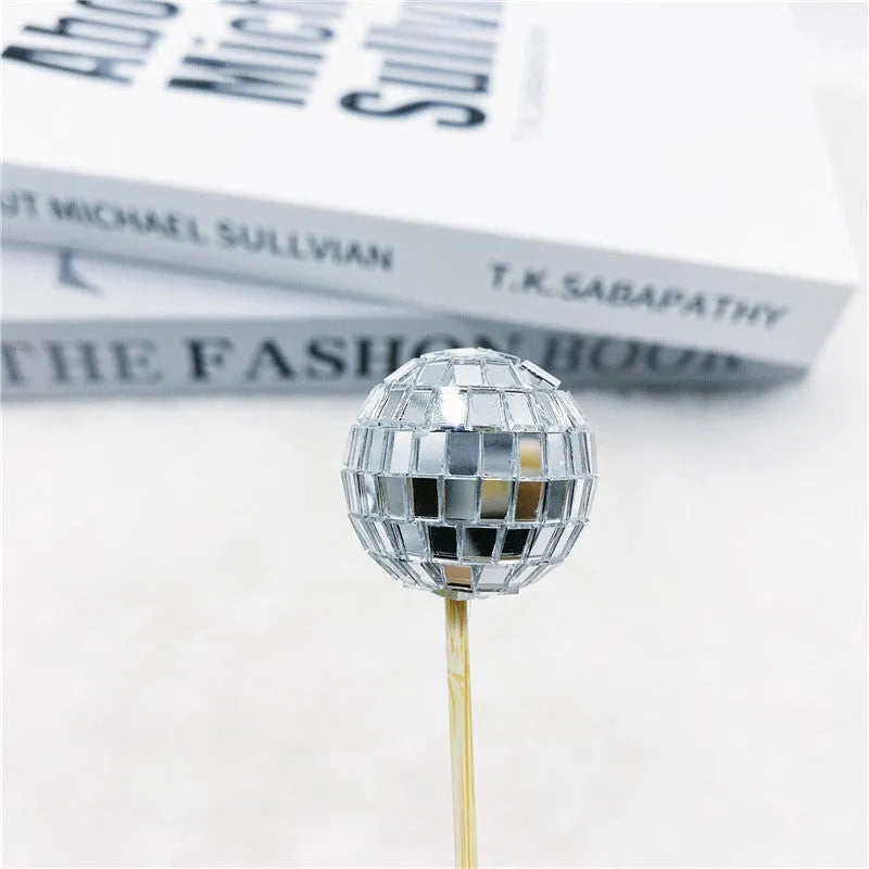 Glass disco ball cake decoration on a wooden stick in various sizes on a cake.