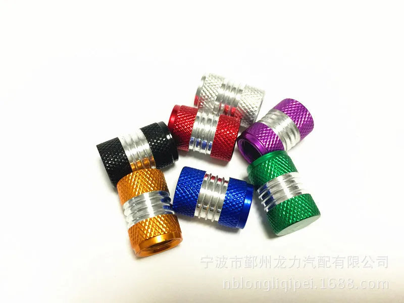 Seven aluminium alloy tyre valve dust caps in black, blue, gold, green, purple, red, and silver on a white background