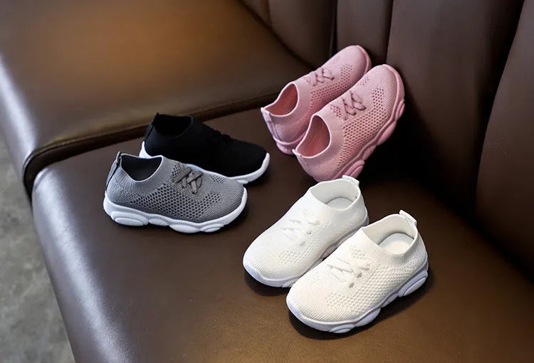Children's white fabric lazy slip-on shoe with non-slip rubber sole on a wooden floor.