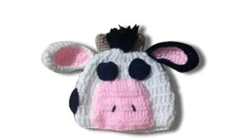 Hand-knitted white baby cow suit set with matching hat and pants on a newborn