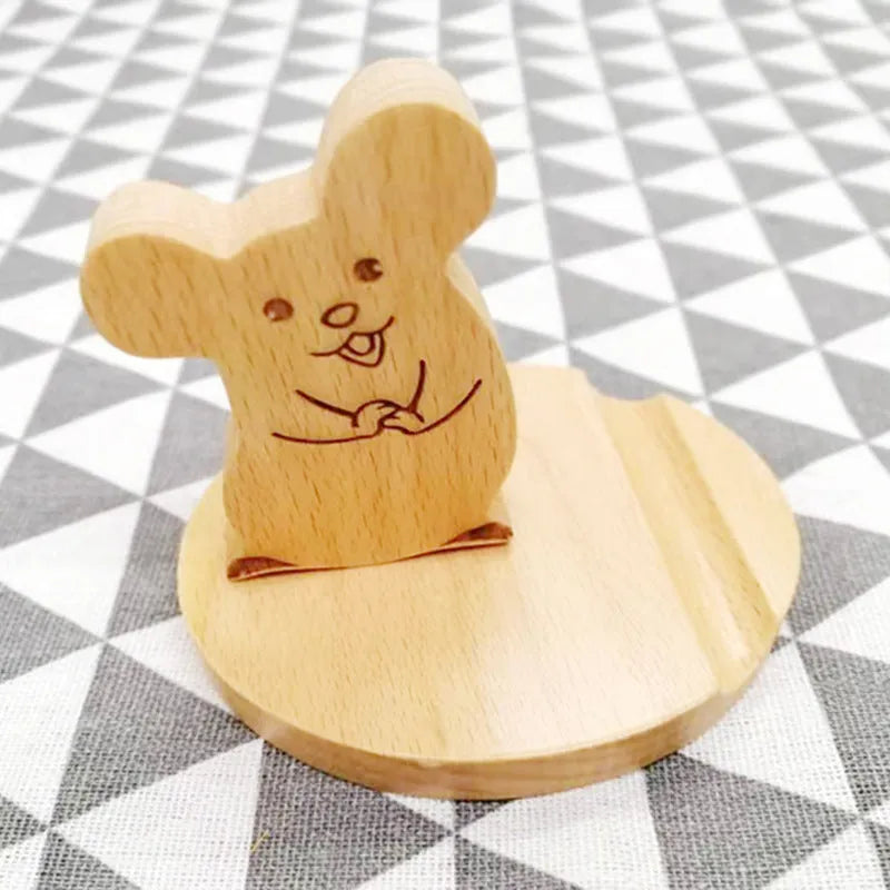 Solid beech wood mobile phone stand with a resin cow figurine and a slot for holding coins on a wooden desk.
